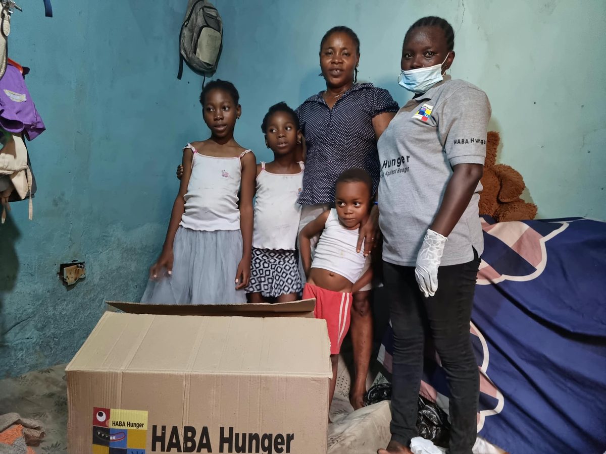 A HABA Hunger volunteer with a mother and her children beside their food support box during a home visit